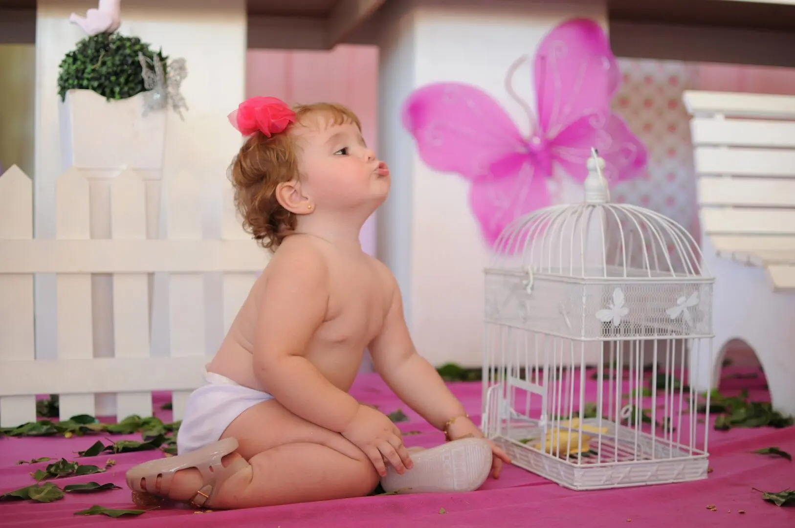 A baby sitting on the ground next to a bird cage.