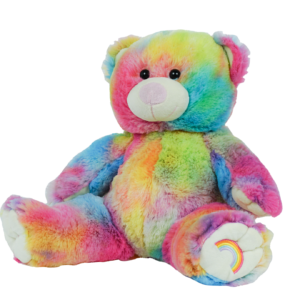 A rainbow colored teddy bear is sitting on the ground.