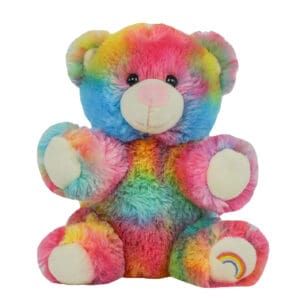 A rainbow colored teddy bear sitting on top of a white table.