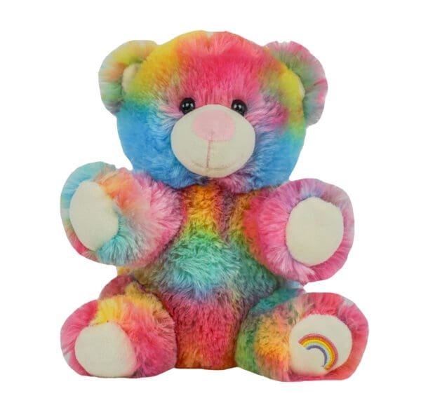 A rainbow colored teddy bear sitting on top of a white table.